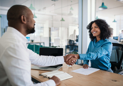 A female business adviser shaking hands across a table with a male businessman