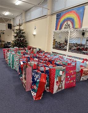 A huge pile of presents in colourful Christmas gift bags with a Christmas tree in the back ground